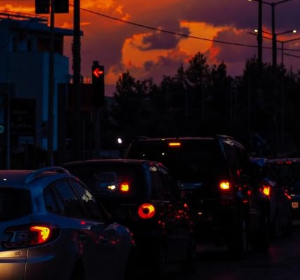 Cars lined up on a street at dusk with a vibrant sunset sky creating a dramatic silhouette scene.